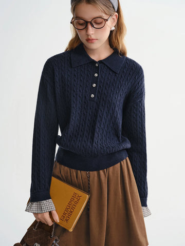 Person wearing a navy blue cable knit sweater and brown skirt, holding a book.