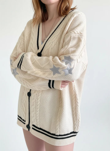 Person wearing a cream-colored cardigan with star designs and black buttons.