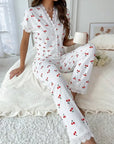 Woman wearing a white pajama set with red cherries sitting on a bed.