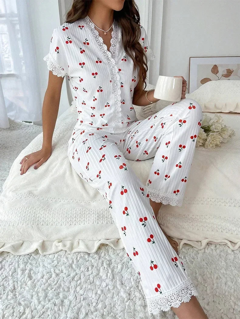 Woman wearing a white pajama set with red cherries sitting on a bed.