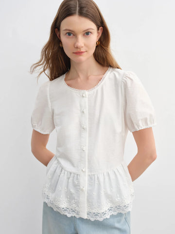 Woman wearing a white blouse with lace details on a plain background