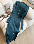Teal cardigan with button details draped over a white armchair with a magazine and handbag.