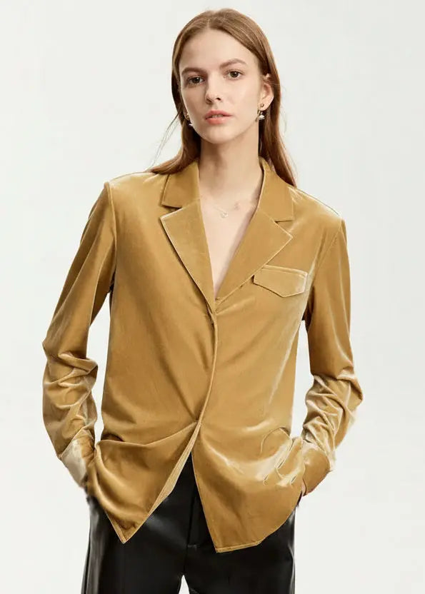 Woman wearing a mustard yellow blazer with a plain background.
