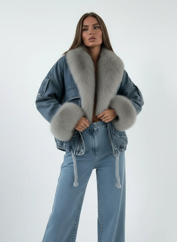 Person wearing a denim jacket with fur trim, sitting on a bed.