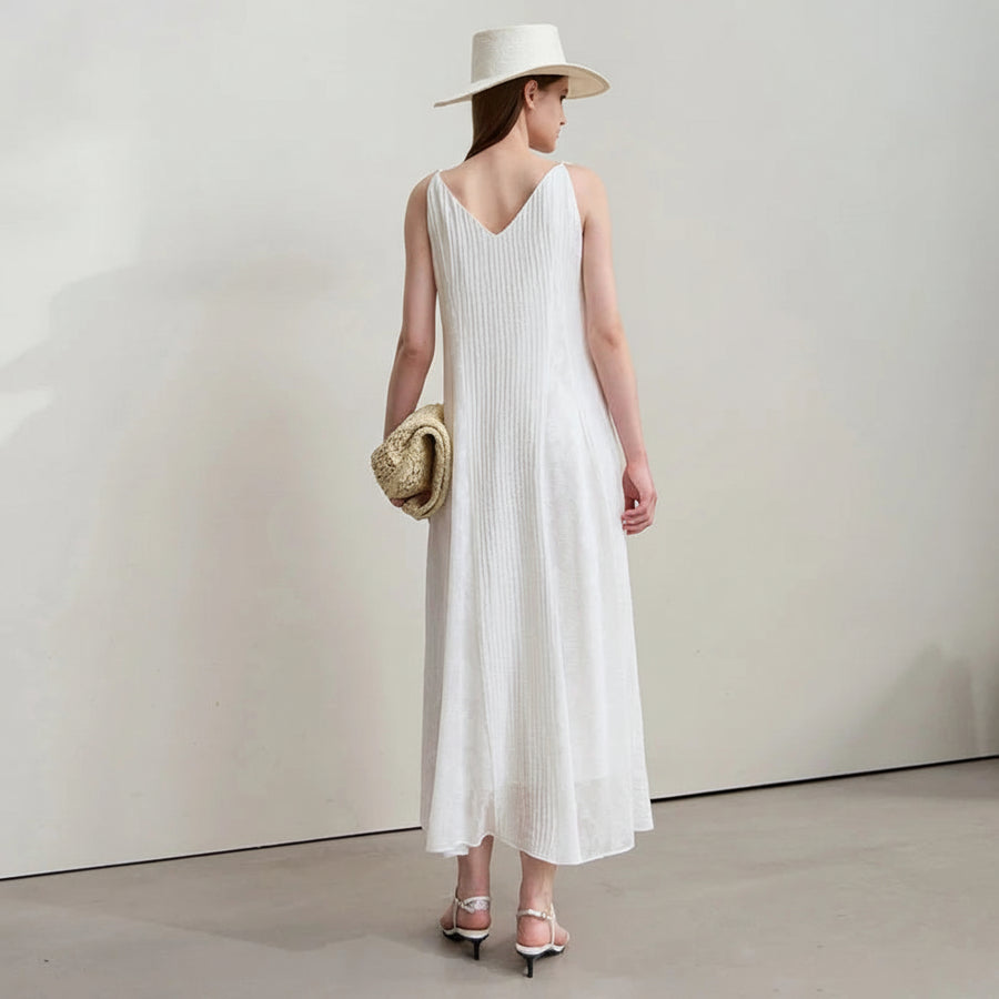 Woman wearing a white dress and hat, holding a straw bag on a plain background with AMII branding.